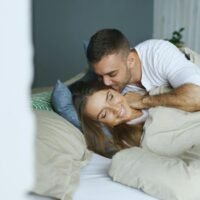 Romantic couple cuddling in bed, evoking warmth and intimacy with soft lighting.